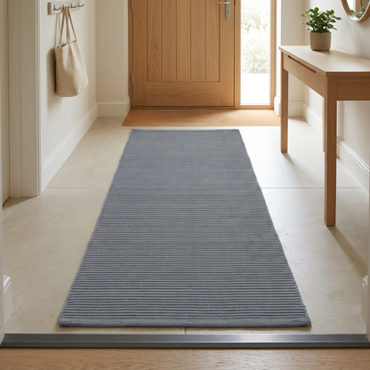 Alfombra gris en una entrada luminosa con puerta de madera clara, planta y consola