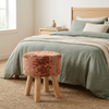 Taburete naranja junto a una cama con textiles verde salvia
